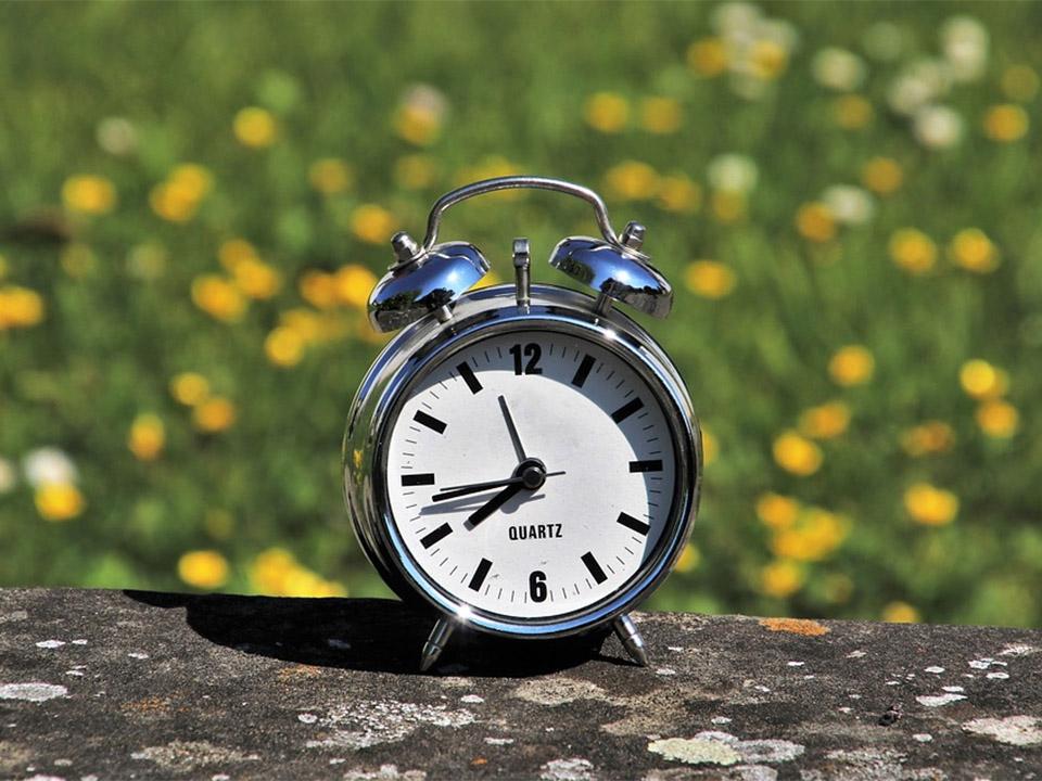 A clock placed on a center part of the table with yellow flowers behind